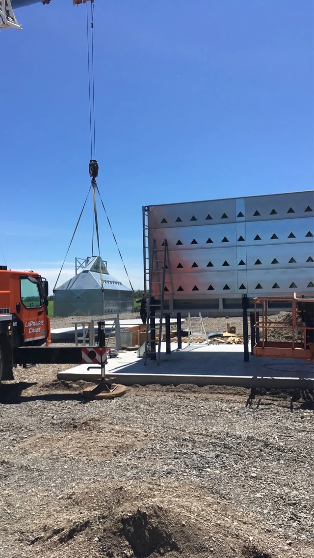 Crane lowering a grain dryer section beside the assembled dryer