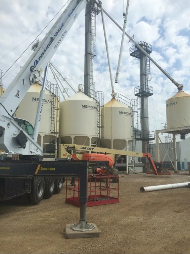 Crane positioning white replacement spouting above a row of hopper bins