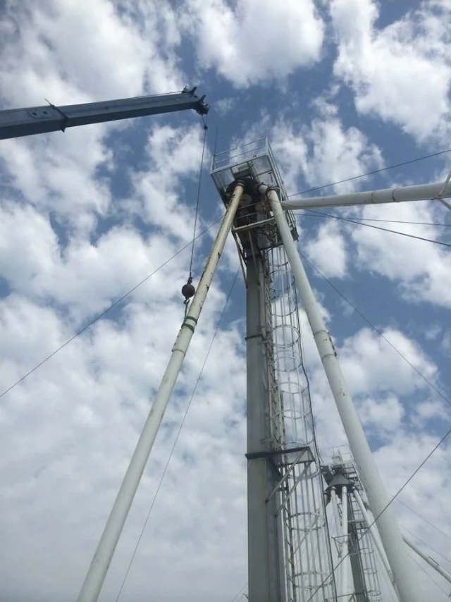 Crane and lifting sling supporting a white spouting section alongside a bucket elevator
